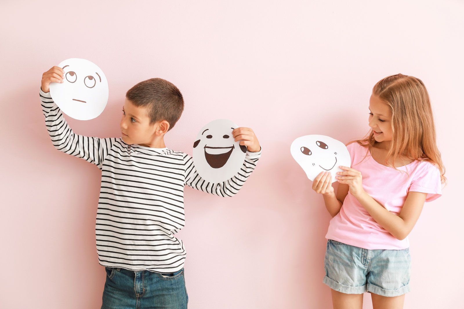 Niña y niño con caricaturas de caras en las manos